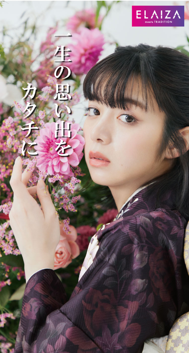 暗い花柄の着物を着た人が、顔の横にピンクの花を持っています。長い黒髪で前髪があります。後ろには、みずみずしいピンクと白の花があります。左側に日本語のテキストが重ねられ、右上隅には「meets TRADITION」というテキストが入った ELAIZA のロゴがあります。.