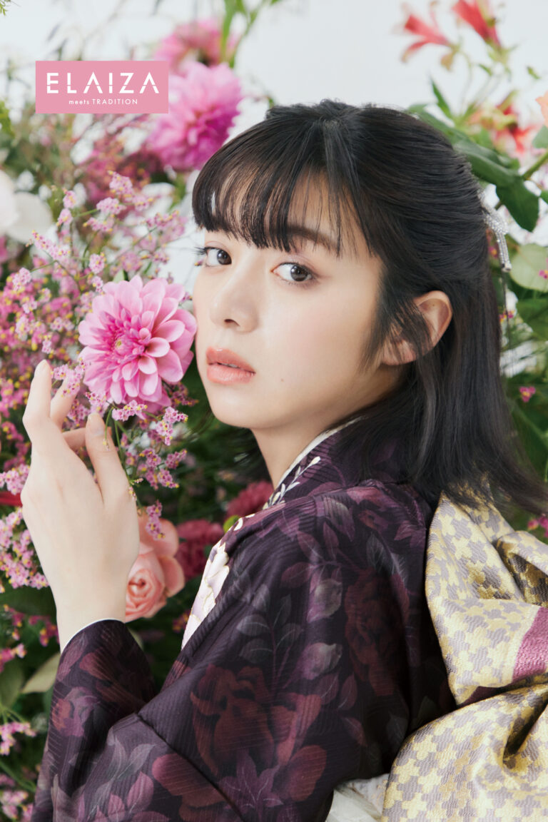 伝統的な紫の花柄の着物を着た若い女性がピンクの花を持っており、背景にはピンク、紫、白の花が鮮やかに飾られています。左上に「EL-721」という文字が見えます。彼女は前髪のある黒髪で、表情は穏やかです。