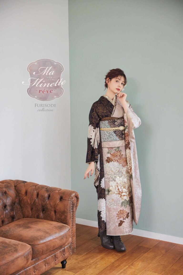 女性が、茶色の革の房飾りソファの近くの明るい緑の壁を背に立っています。彼女は、黒、金、ベージュの色合いの花柄と幾何学模様が描かれた細かい振袖を着ています。髪はアップにまとめられ、片手で顎を触ってポーズをとっています。壁には「Ma Minette rêve FURISODE collection」という文字が書かれています。