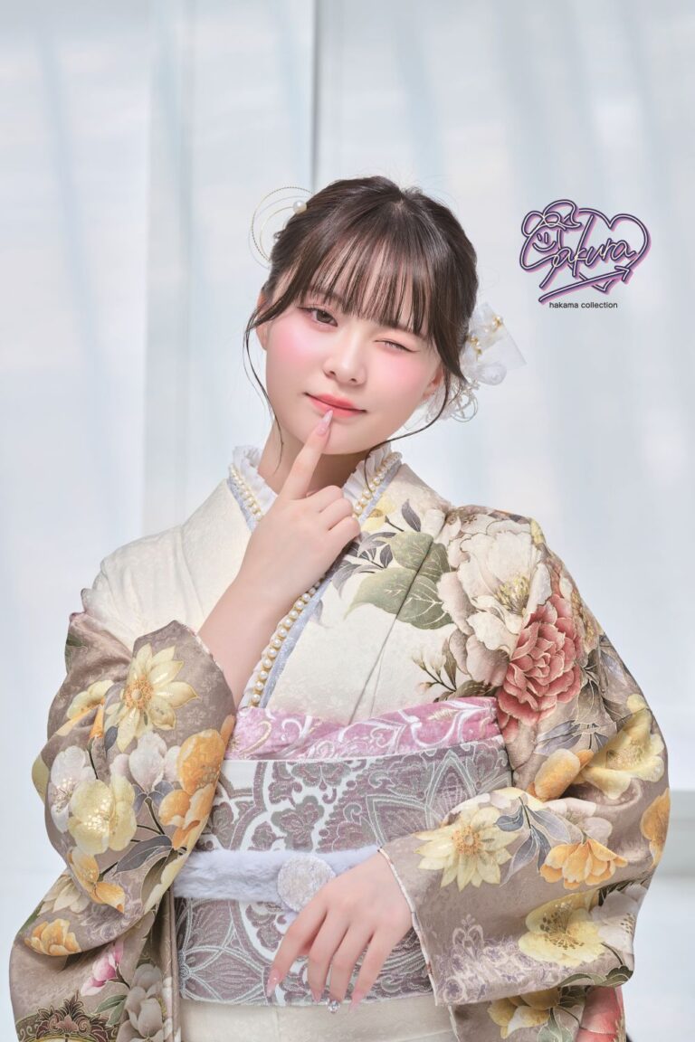 淡いパステルカラーの花柄の着物を着た人物が、明るい背景に立っています。黒髪を短く切り、花のアクセサリーを飾り、指で頬を触りながらウインクしています。右側には「さくら」と「はかまコレクション」の文字が紫色で書かれています。.