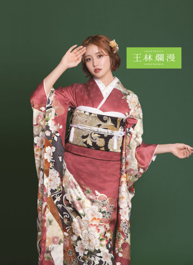 栗色を基調とした花柄の着物を着た女性が、緑の背景に立っています。短いウェーブヘアに花が飾られています。片方の手は額に触れ、もう片方の手は横に伸ばされています。画像の右側にテキストがあります。.