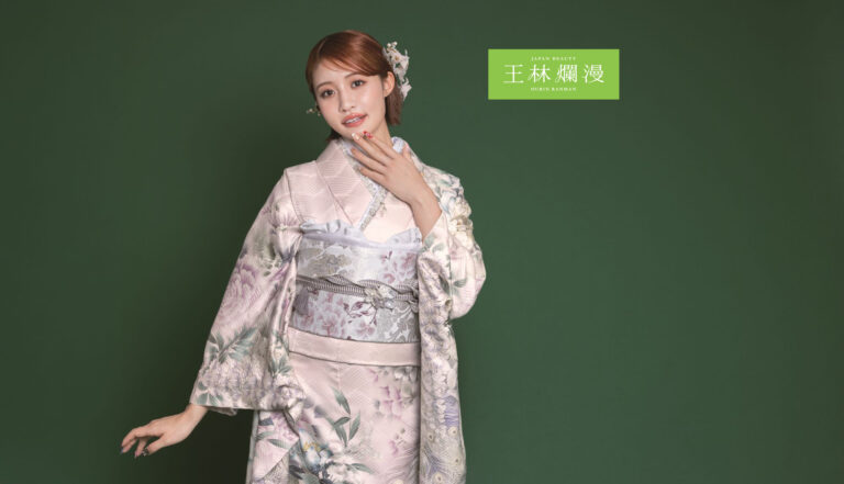 花柄の着物を着た女性が、緑の背景にポーズをとっています。着物は薄紫とグレーの色合いで、複雑な模様が施されています。髪は整えられ、花で飾られています。彼女は片手で顎をそっと触っています。画像には中国語の文字が書かれています。.