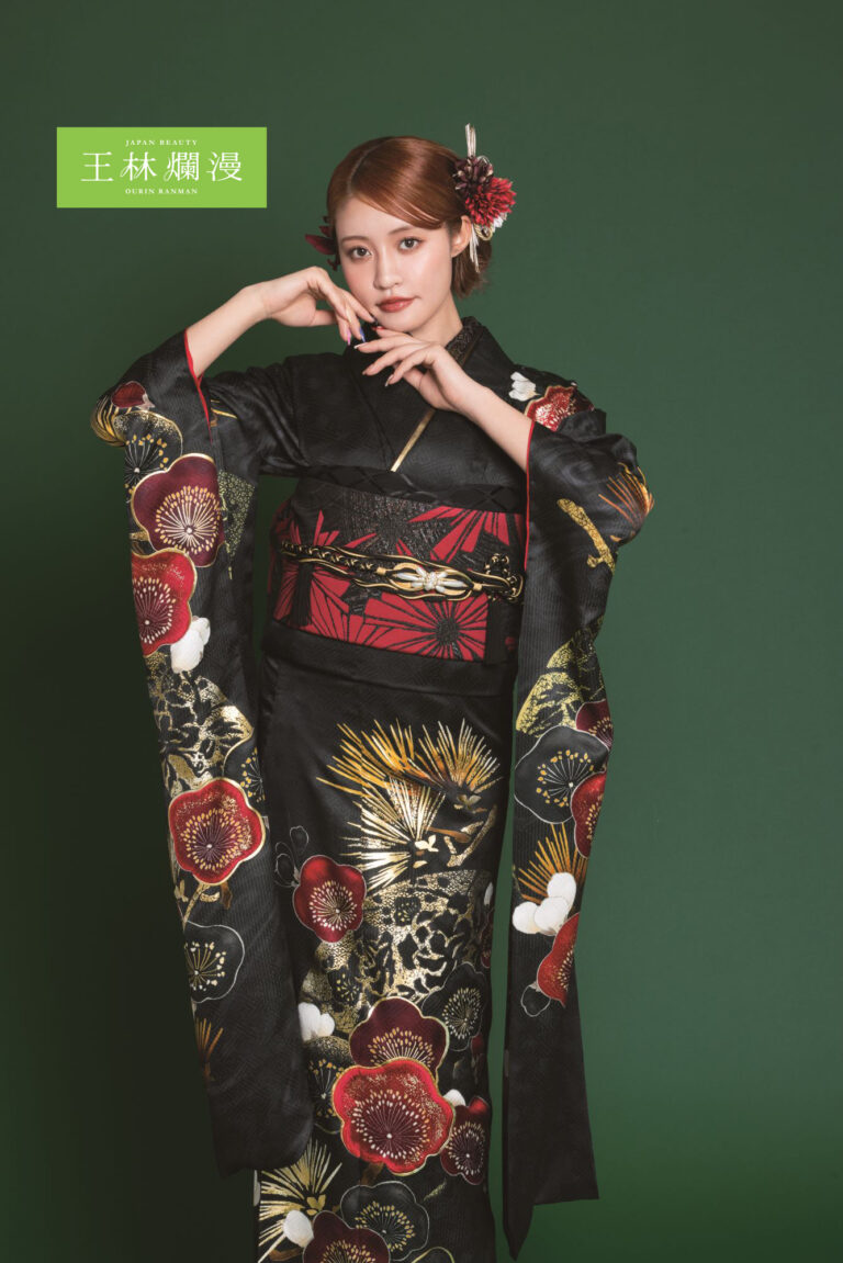 濃い緑色の背景に、赤、金、白の鮮やかな花柄が描かれた黒い着物を着た女性がポーズをとっています。花の髪飾りをつけ、両手は顔の近くに優雅に置かされています。衣装には、金と黒のディテールが施された赤い帯があしらわれています。.