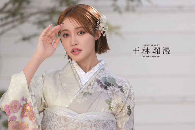 花柄の着物を着た人物が、右手を頭の近くで上げてポーズをとっています。茶色の短い髪に、飾りのかつらをつけています。背景には、緑が少しある明るい色の壁があります。右側には、「Japan Beauty」と「Oren Ranman」の文字があります。.