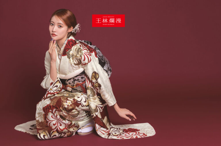 女性が栗色の背景にひざまずいています。彼女は、赤、白、茶色の複雑な花柄が描かれた伝統的な着物を着て、エレガントなアップスタイルで髪をまとめ、片手を顔の近くに持ってポーズをとっています。白いソックスとサンダルでこのスタイルは完成しています。上部に赤い文字が見えます。.