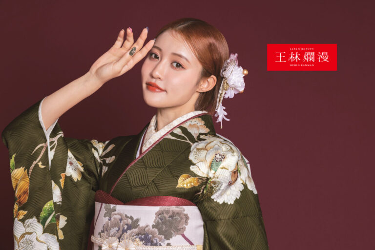 花柄の着物を着た女性が、額の近くに手を挙げて、濃い赤の背景にポーズをとっています。彼女は花の付いた精巧なヘアピースをつけています。着物には複雑な白と黄色の模様が描かれています。右上隅には、赤い四角の中に白い漢字が書かれています。.