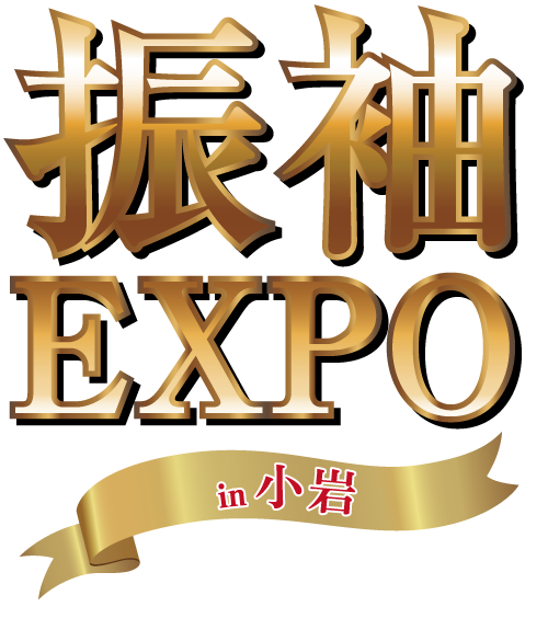 この画像では、「EXPO」という文字の上に、太字で光沢のある金色の文字で「振袖」という金色の漢字が描かれています。その下には、赤い日本語の文字で「in 小岩」と書かれた金色のリボンが表示されています。背景は黒で、文字とリボンが目立っています。.