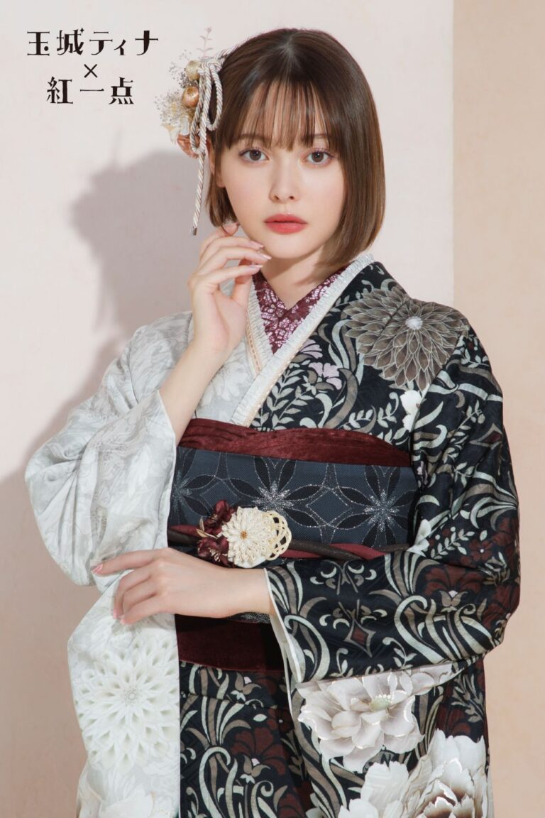 黒、白、栗色の複雑な花柄が描かれた日本の伝統的な着物を着ている人物。花とリボンをあしらった装飾的なかつらをつけた短い髪をしている。背景は柔らかいベージュ色。.