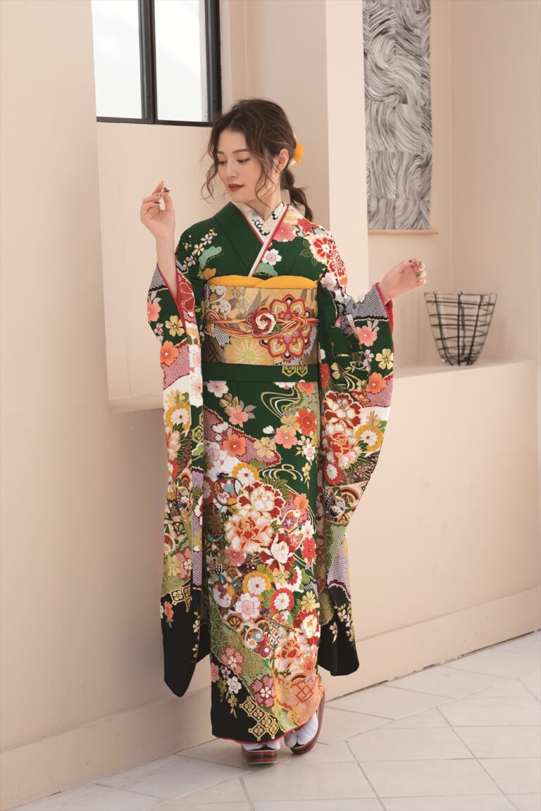 緑色の地に複雑な模様が入った、色鮮やかな花柄の着物を着た女性が室内に立っている。花を手に持ち、うつむき、黄色のアクセサリーで髪をまとめている。彼女の背後には窓があり、抽象的なアート作品が飾られ、棚にはワイヤーバスケットが置かれている。.