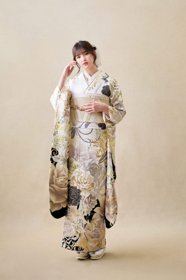 ベージュの背景に、クリーム色と金色の繊細な花柄の着物を着た若い女性が立っています。黒髪をまっすぐに伸ばし、かつらを飾り、両手を優しく前に組んでいます。落ち着いた表情で、白い草履を履いています。.